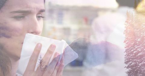Woman sneezing while holding tissue overlaid with winter scenery