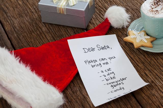 Handwritten letter to Santa Claus placed on a wooden table alongside a Santa hat and a gift box. Ideal for holiday-themed promotions, Christmas greeting cards, festive blog posts, and social media content celebrating the holiday season.