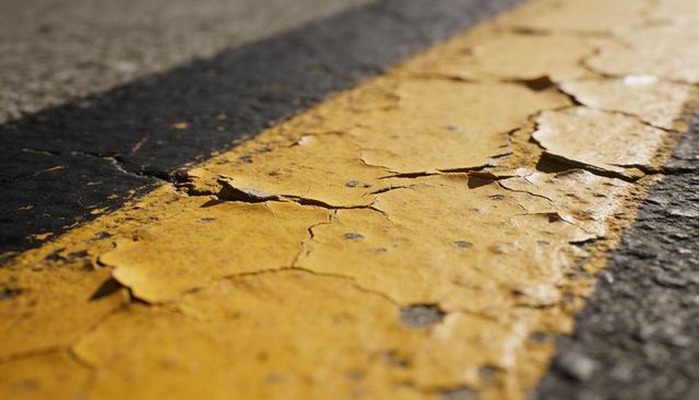 Peeling yellow road line revealing cracked asphalt texture sunlit closeup diagonal