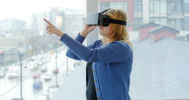 The image shows a young woman wearing a VR headset, fully immersed in a virtual experience in a modern office environment. Ideal for use in technology blogs, articles about virtual reality and augmented reality, workplace innovation, and tech-related marketing materials.