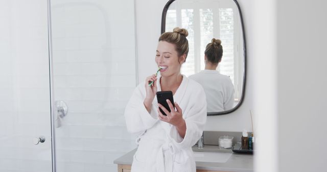 Woman in White Bathrobe Brushing Teeth While Looking at Smartphone - Download Free Stock Images Pikwizard.com