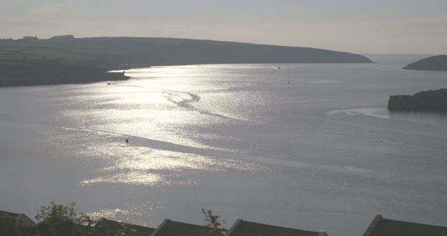 Serene Water Surface Reflecting Sunlight at Dusk with Coastal Landscape in Background - Download Free Stock Images Pikwizard.com