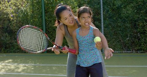 Mother and Daughter Learning Tennis Together Outdoors