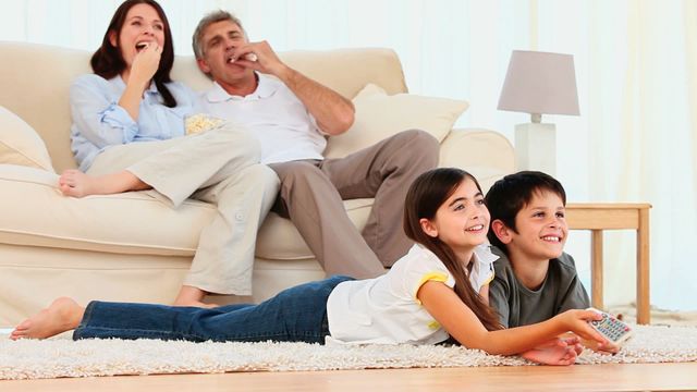 Family relaxing together, smiling while watching television. Shows bond, happiness, perfect for promoting home products, family services, or lifestyle content.