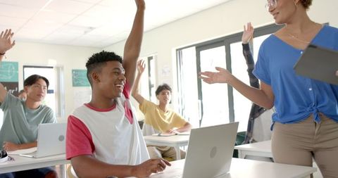 High School Students in Classroom Engaging with Teacher Using Laptops
