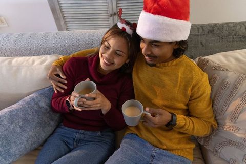 Couple cuddling on sofa sipping hot drinks during cozy Christmas evening