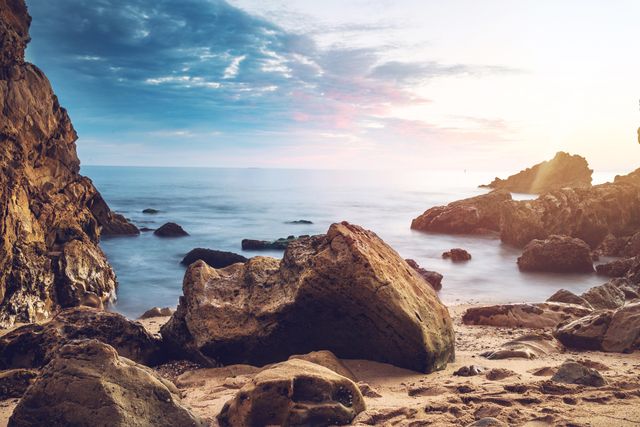 Scenic rocky beach during sunset with tranquil waves and a serene atmosphere. Ideal for promoting travel destinations, nature blogs, meditation resources, and coastal vacation advertisements.