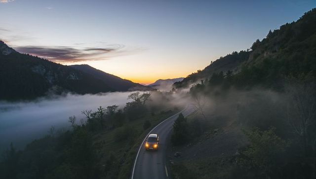 Compact car driving through misty mountain valley at sunrise on winding ridge road