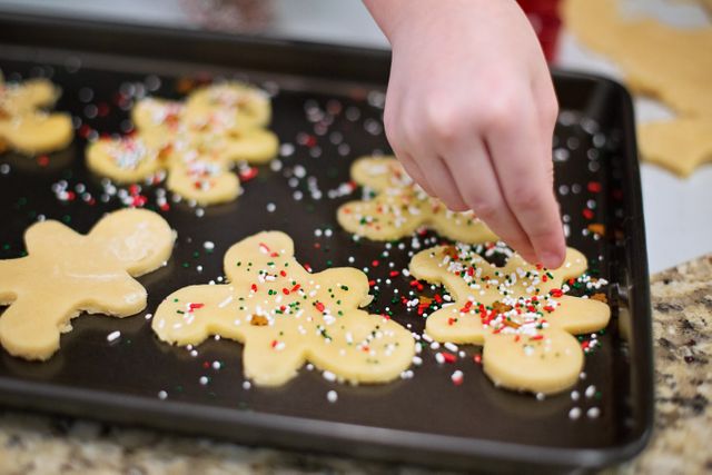 Child adding colorful sprinkles to holiday cookies in baking tray, ideal for festive season promotions, Christmas cooking classes, family activity ideas, and baking recipe blogs.