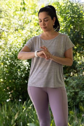 Woman checking smartwatch in leafy garden during outdoor fitness routine
