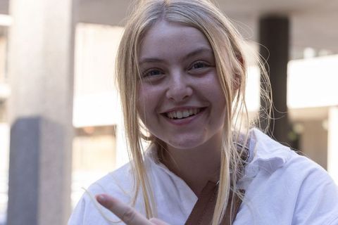 Young woman smiling and pointing at camera in urban courtyard hoodie lifestyle portrait