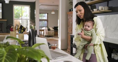 Mother Multitasking with Laptop at Kitchen Island Holding Baby