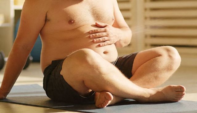 Plus-size man doing seated yoga on mat in sunlit studio embracing body positivity
