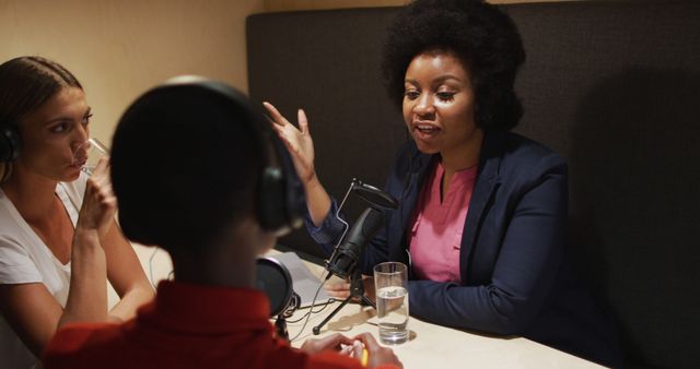 Image shows a diverse group of individuals passionately recording a podcast in a cozy studio. Ideal for use in content promoting podcasting, audio production, media collaborations, communication skills, interview setups, and showcasing team diversity.
