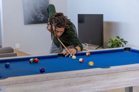 Adult african american man lining up pool shot on blue-felt table in modern living room