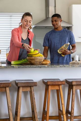 Couple preparing healthy meal at granite kitchen island with fruit bowl and cooking oil