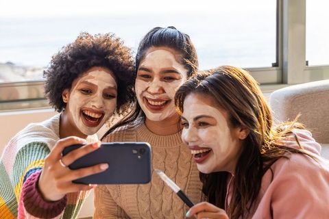 Women taking selfie during pamper night with clay face masks on cozy coastal sofa