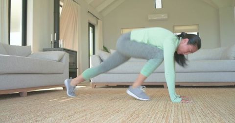 Asian woman doing mountain climber exercise in sunlit minimalist living room on woven rug
