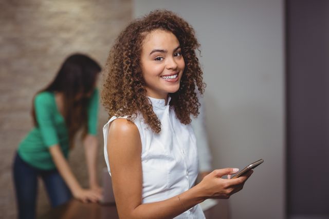 Smiling female executive holding a tablet in a modern office. Ideal for use in business, technology, and professional workplace contexts. Suitable for illustrating teamwork, corporate culture, and digital device usage in a professional setting.