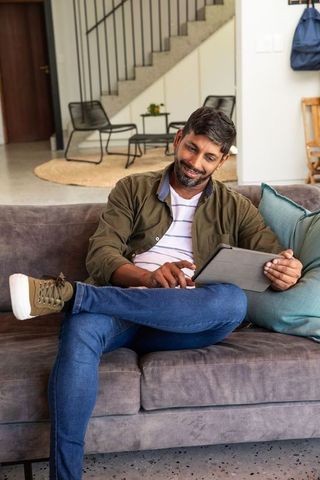 Smiling Man Relaxing on Sofa Using Digital Tablet at Home