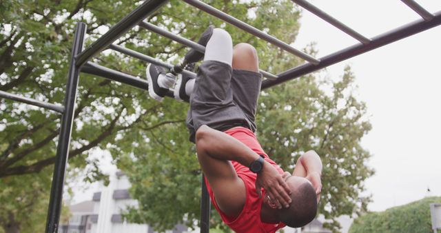 Biracial man exercising on climbing frame with his prosthetic leg in park. Sport, active lifestyle and disability.