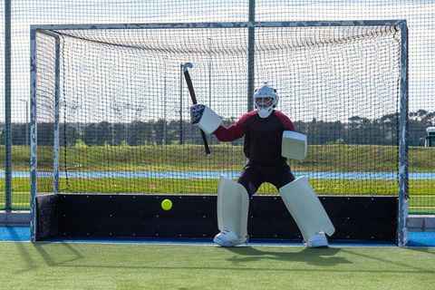 Field hockey goalie defending net with stick and protective gear