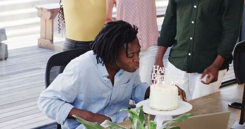 Young Professional Blowing Out Candles in Office Birthday Celebration