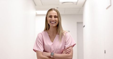 Smiling female nurse wearing pink scrubs standing confidently in bright clinic corridor
