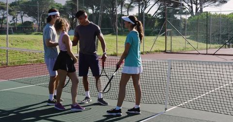 Diverse players meeting at tennis net on sunny outdoor hard court during friendly match