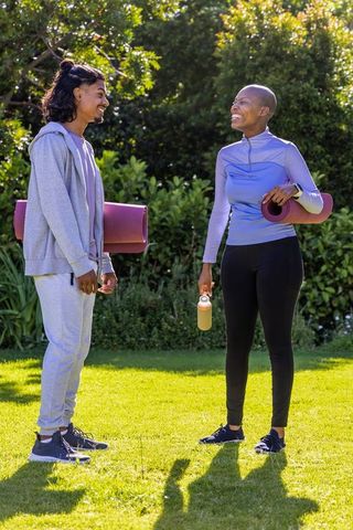 Sunlit outdoor yoga buddies laughing and carrying mats in park wellness lifestyle