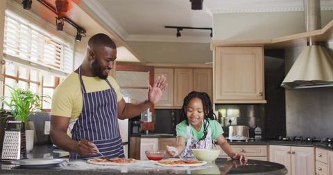 Smiling father guiding daughter making homemade pizzas together in modern family kitchen