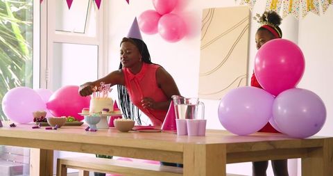 Woman adding finishing touches to birthday cake with pink theme