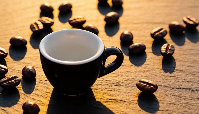 Black espresso cup glowing in warm golden light with scattered roasted coffee beans