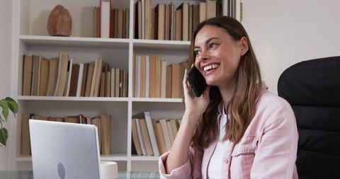 Businesswoman communicating on phone in home office with laptop