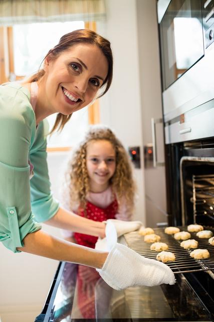 Mother and daughter enjoying a baking session in a modern kitchen. Perfect for illustrating family activities, cooking tutorials, parental bonding, and home life.