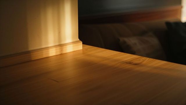 Sunlight bathing honey wooden tabletop with warm grain, trim highlight and soft bedroom shadows