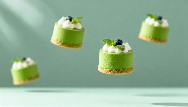 Floating green matcha mousse cakes with blueberry and mint on minimalist emerald backdrop