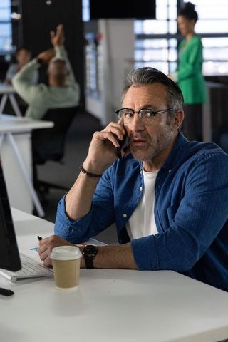 Middle-aged businessman making urgent phone call in modern open-plan office with coworkers