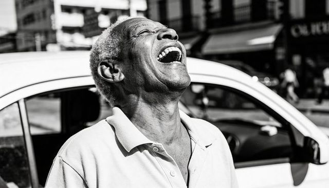 Joyful senior man laughing with head tilted back beside open car door on urban street