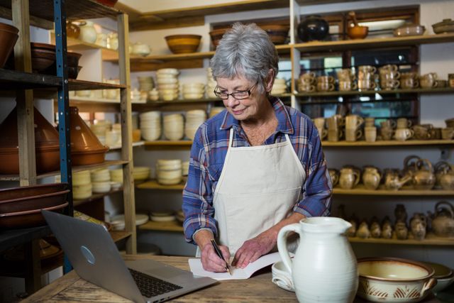 Female potter making note from laptop in pottery shop