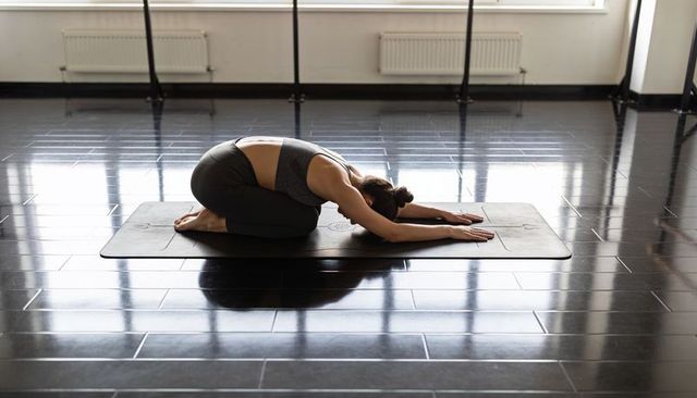 Woman practicing child's pose on mat in minimalist yoga studio with natural light