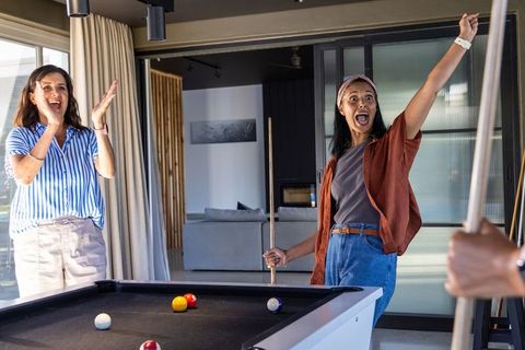 Multicultural friends celebrating winning shot while playing pool in modern home