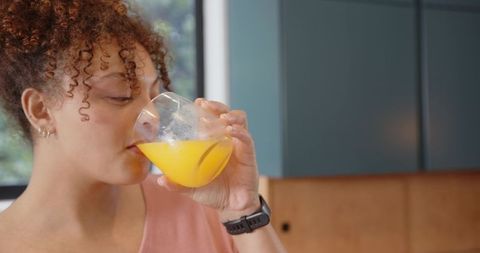 Young woman drinking fresh orange juice in modern kitchen closeup profile with wristwatch