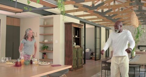 Senior African man and woman chatting in contemporary open-plan kitchen with exposed beams