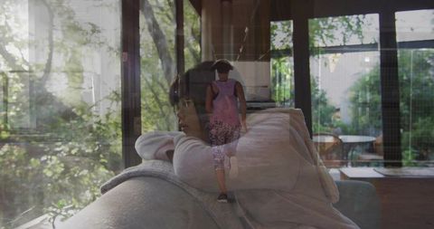 Caregiver resting on couch reflecting walking child in window glass double exposure
