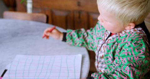 Young boy coloring at round table in bright room