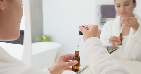 Woman applying skincare serum in minimalist bathroom mirror reflection