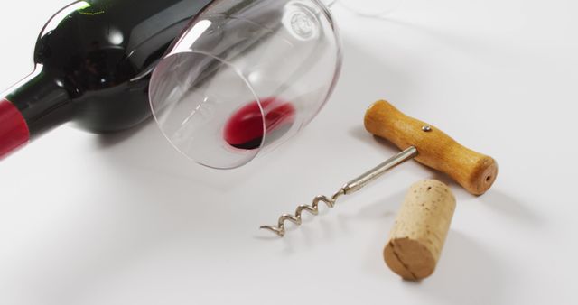 Red wine bottle, empty glass, cork and corkscrew lying on white surface with copy space. Wine, alcohol, beverage and wine tasting concept.