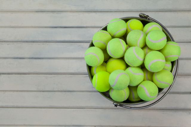 Overhead view of tennis balls in metallic bucket on white wooden table