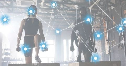 Backlit fitness partners stepping onto plyo boxes holding dumbbells in industrial gym